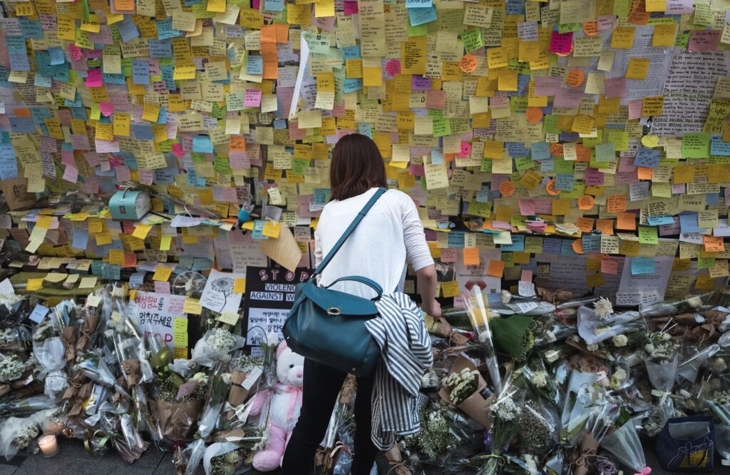 Eine Wand voller beschriebener Post-Its, darunter Blumen und Kuscheltiere, die Menschen im Angedenken an das Opfer des U-Bahnhof Gangnam Mordes 2016 hinterlegt haben.